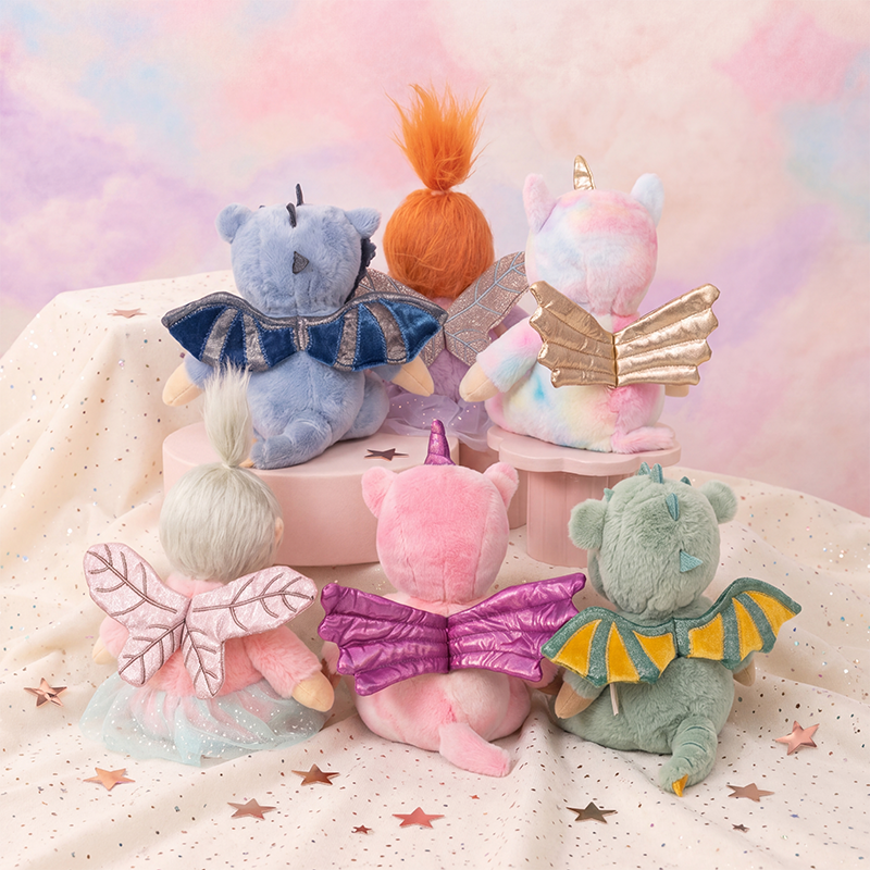 Collection of colorful fairy-themed plush toys on a soft surface with a pastel background.