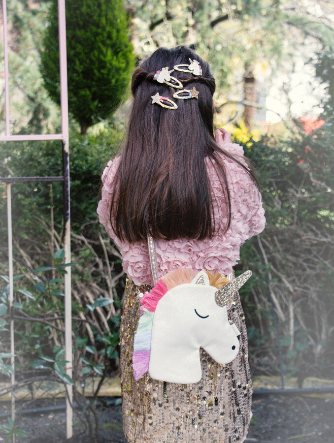 Child with decorative hair clips and a unicorn backpack in an outdoor setting from Rockahula kids
