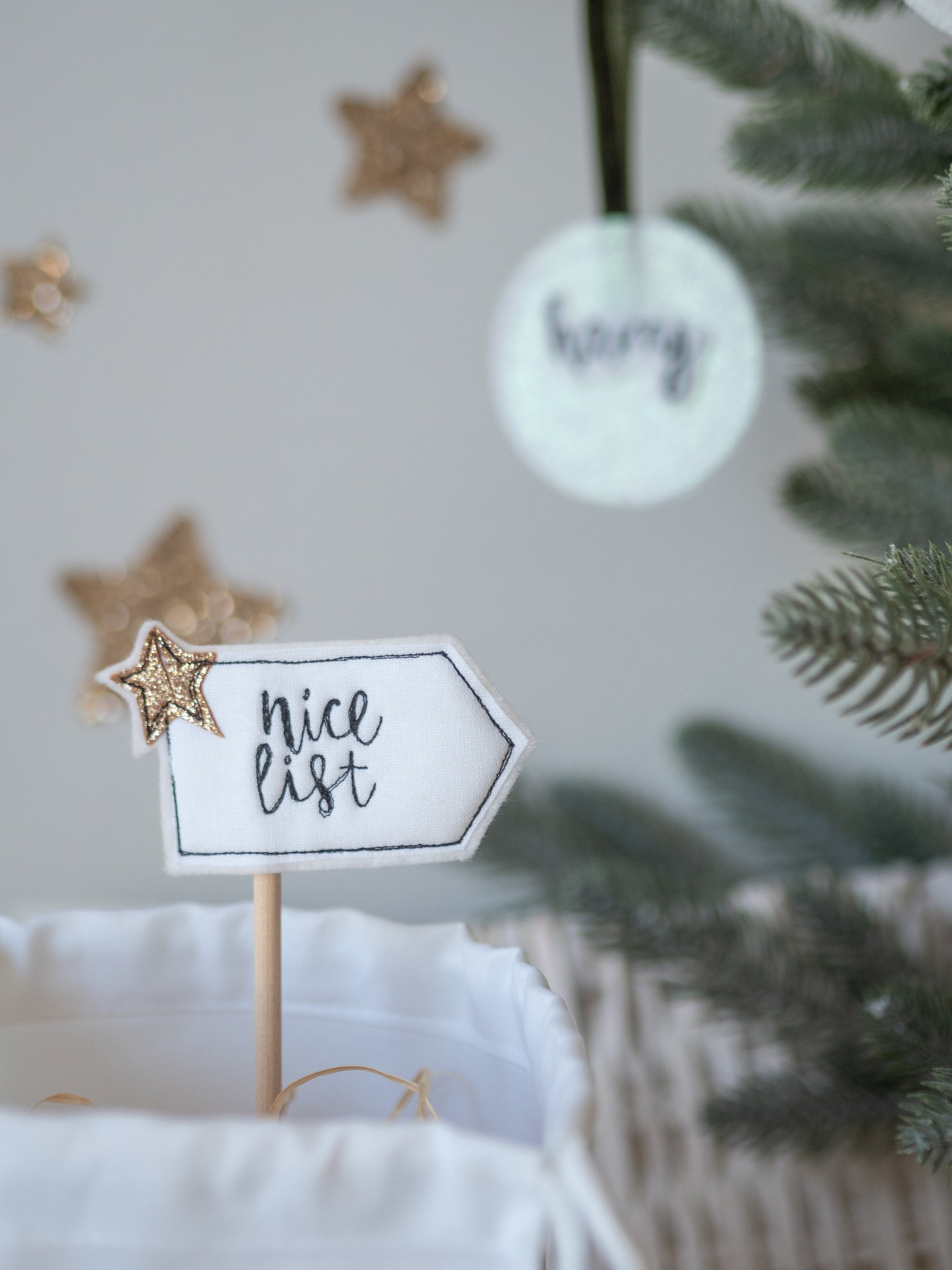 Decorative sign with 'nice list' text on a white surface fabric with Christmas decorations in the background. Girl Friday Embroidery hand stitched mini flag.