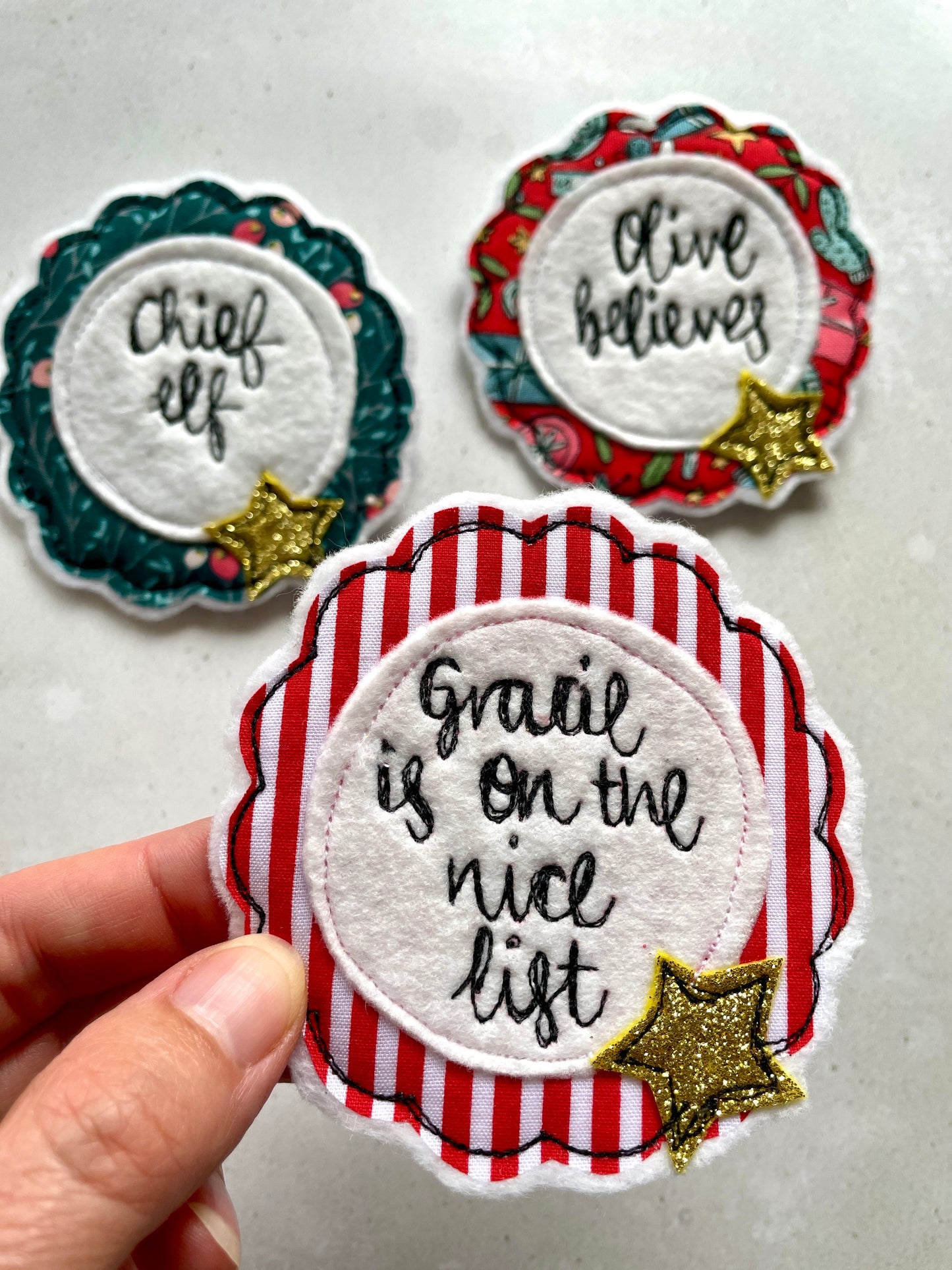 Three decorative patches with text and star embellishments. Childrens personalised name badge with name is on the nice list, Christmas nice list badge with red stripes hand embroidered by Girl Friday Embroidery at Mouse in a Box