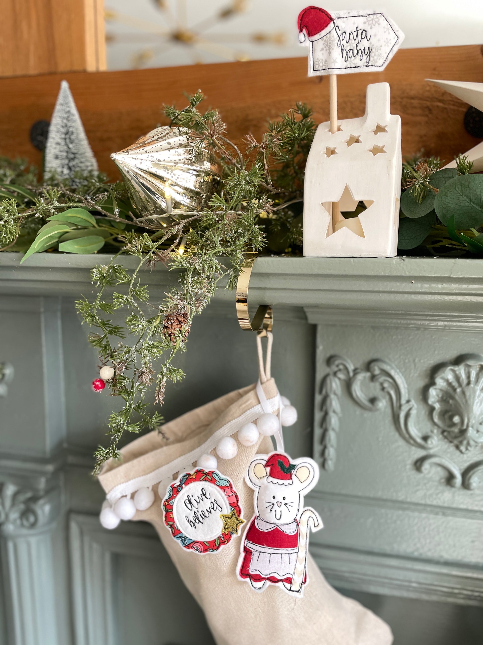 Christmas stocking with decorative I'm a believer Christmas gift badge on a mantel with greenery and a lantern. Children's believer in Christmas badge