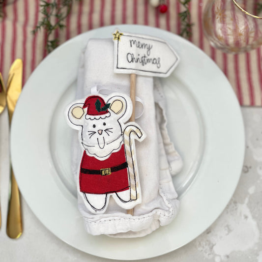 Christmas-themed mouse decoration on a white plate with a striped tablecloth in the background. Hand stitched mouse decoration by Girl Friday Embroidery at Mouse in a box 