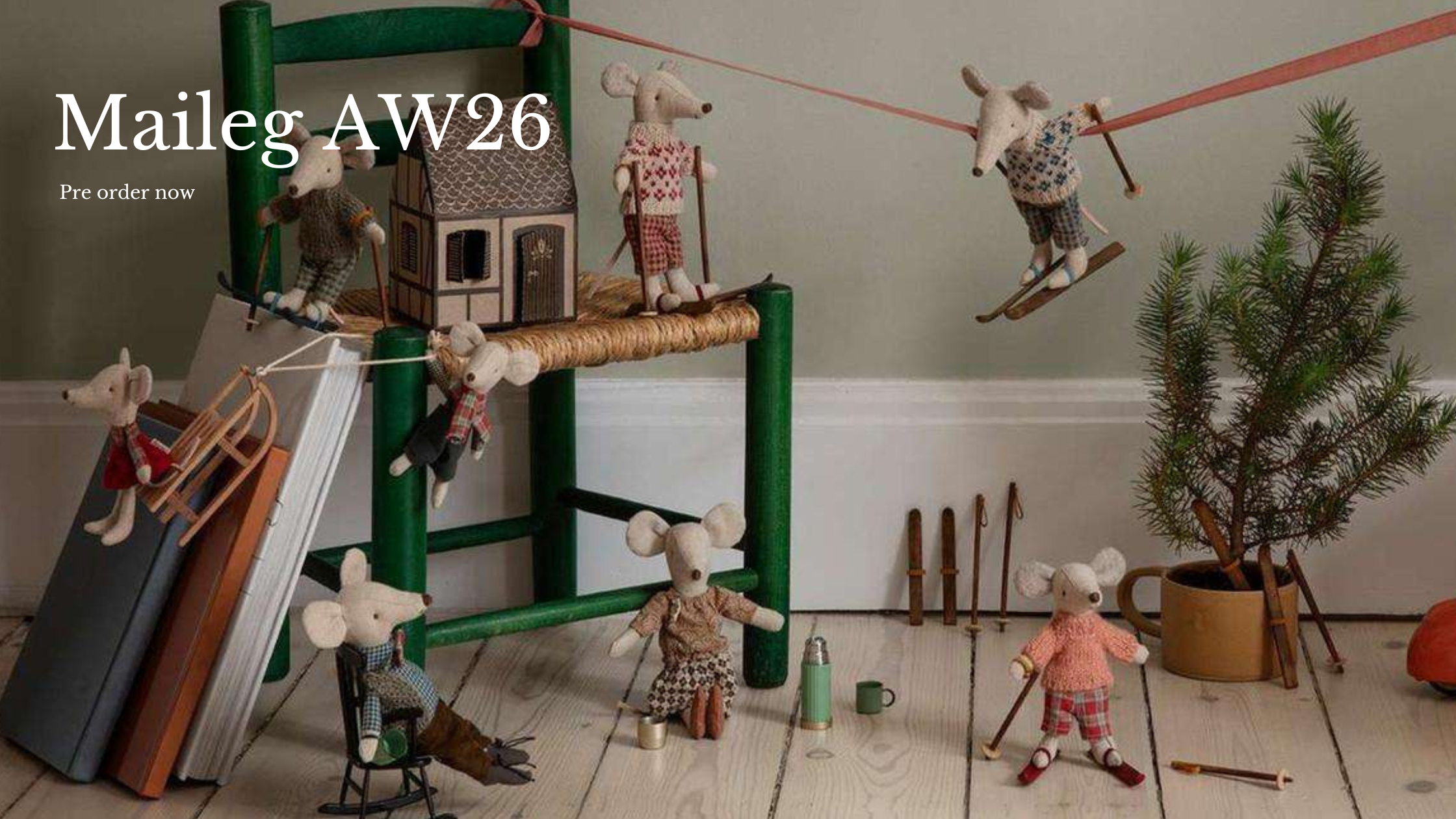 A styled product display for Maileg AW26 pre-order items, featuring a collection of handcrafted plush Maileg mouse toys dressed in winter clothing, arranged around a green wooden chair.