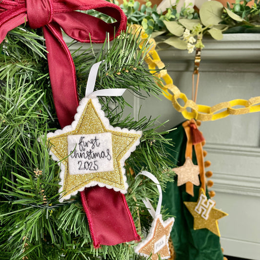 Star-shaped ornament with 'First Christmas 2025' text on a decorated tree. Girl Friday Embroidery Personalsied First Christmas Star Decoration