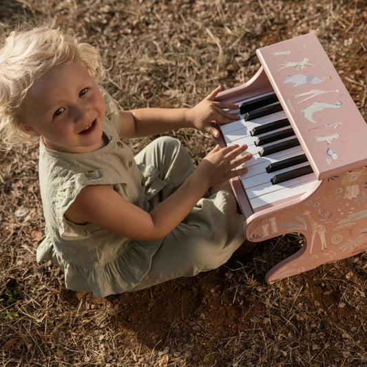 Child playing a pink toy piano outdoors on dry grass